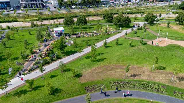 Aerial view: Park mit Wegen, Grünflächen und wenigen Spaziergängern, dahinter Industriegebiet.