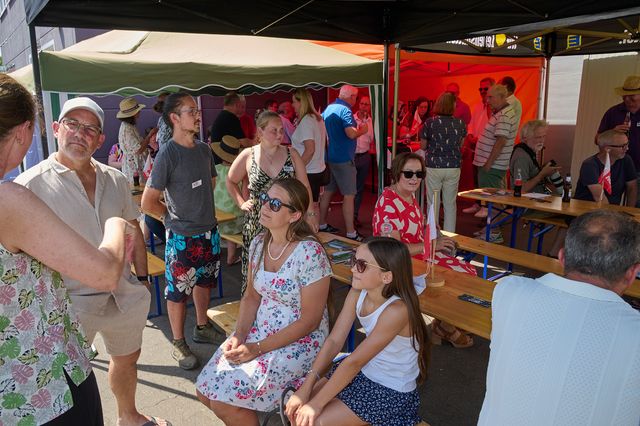 Lebhafte Gruppe genießt Marktbesuch unter Sonnenschirmen mit Ständen und Sitzgelegenheiten.
