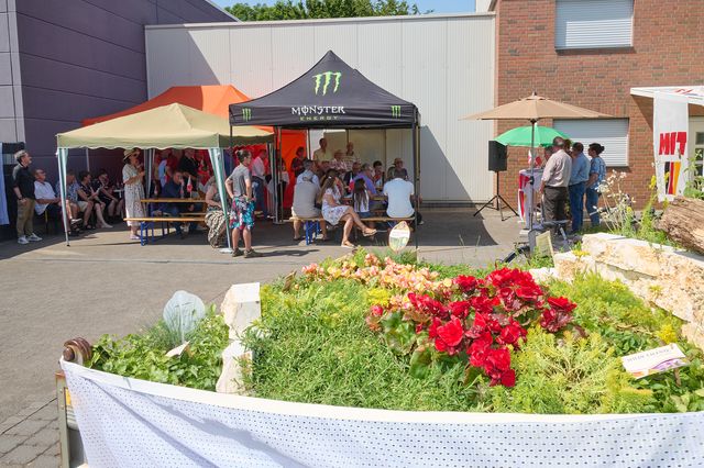 Lebhafte Marktstände mit Blumenbeeten und Besuchern vor einem Gebäude.