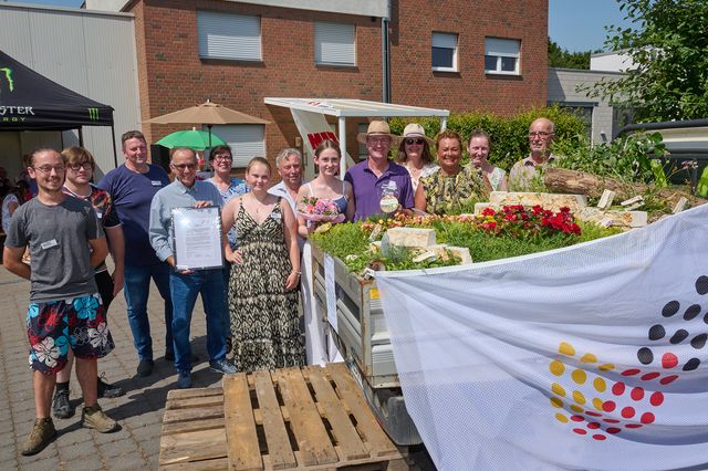 Gruppe von Menschen bei Erntefest mit Blumen und Gemüse auf Marktstand.