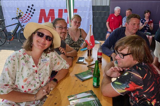 Fröhliche Gruppe sitzt bei Bier und plaudert unter Sonnenschirmen.