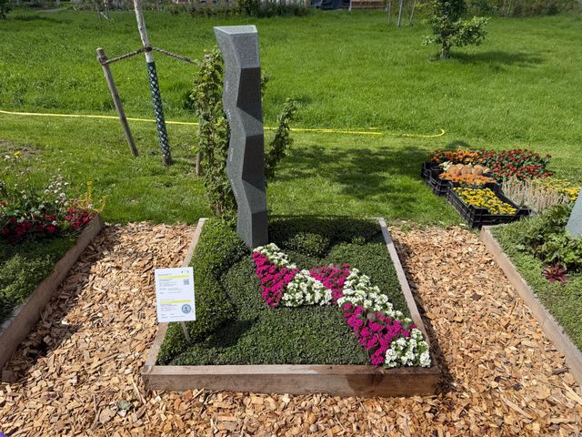 Grabstätte mit gepflegter Bepflanzung und Blumen in einem gepflasterten Beet.