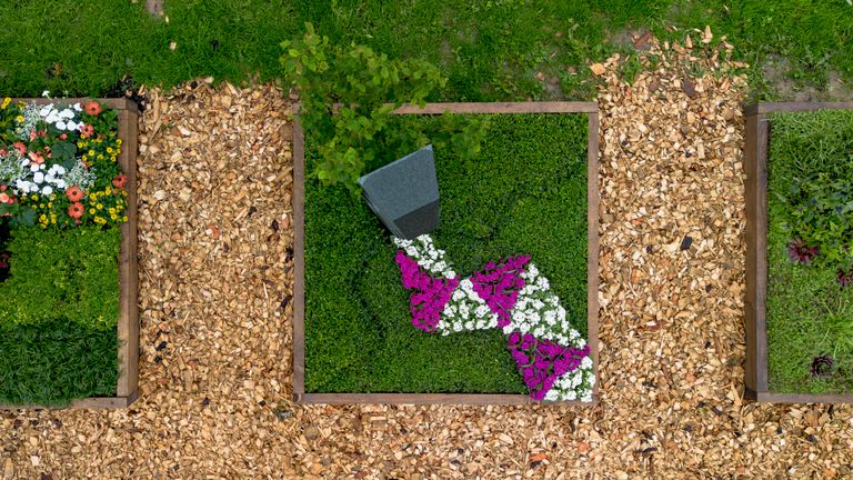 Kreativ bepflanzte Buchstaben „I ❤️ U“ mit Blumen und Mulch in einem Gartenbeet.