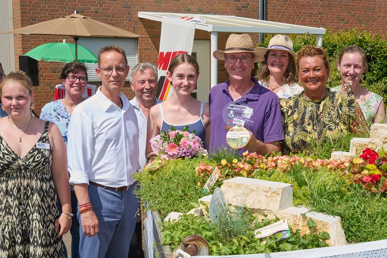 Gruppe von Menschen bei einer Feier mit Kuchen und Blumen-Deko vor Haus.