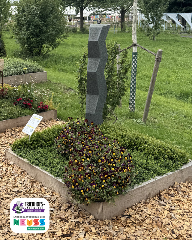 Moderne Skulptur im Garten mit rot-grünen Kugeln und geometrischen Elementen.